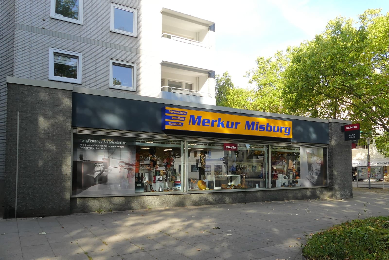 Ladenfront von Merkur Misburg in der Waldstraße mit gelbem Schild und langer Schaufensterzeile