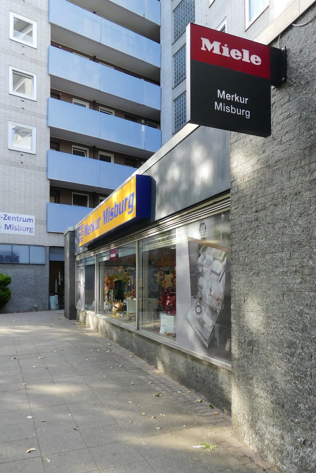 Seitenfront des Geschäfts mit Miele-Ausleger und dem Merkur-Schild
