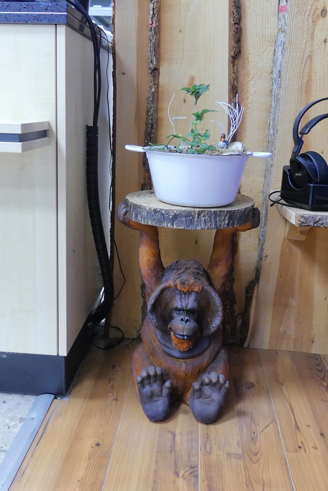 Holzfigur eines Orang-Utans, der einen Blumentopf auf einem Baumstamm trägt