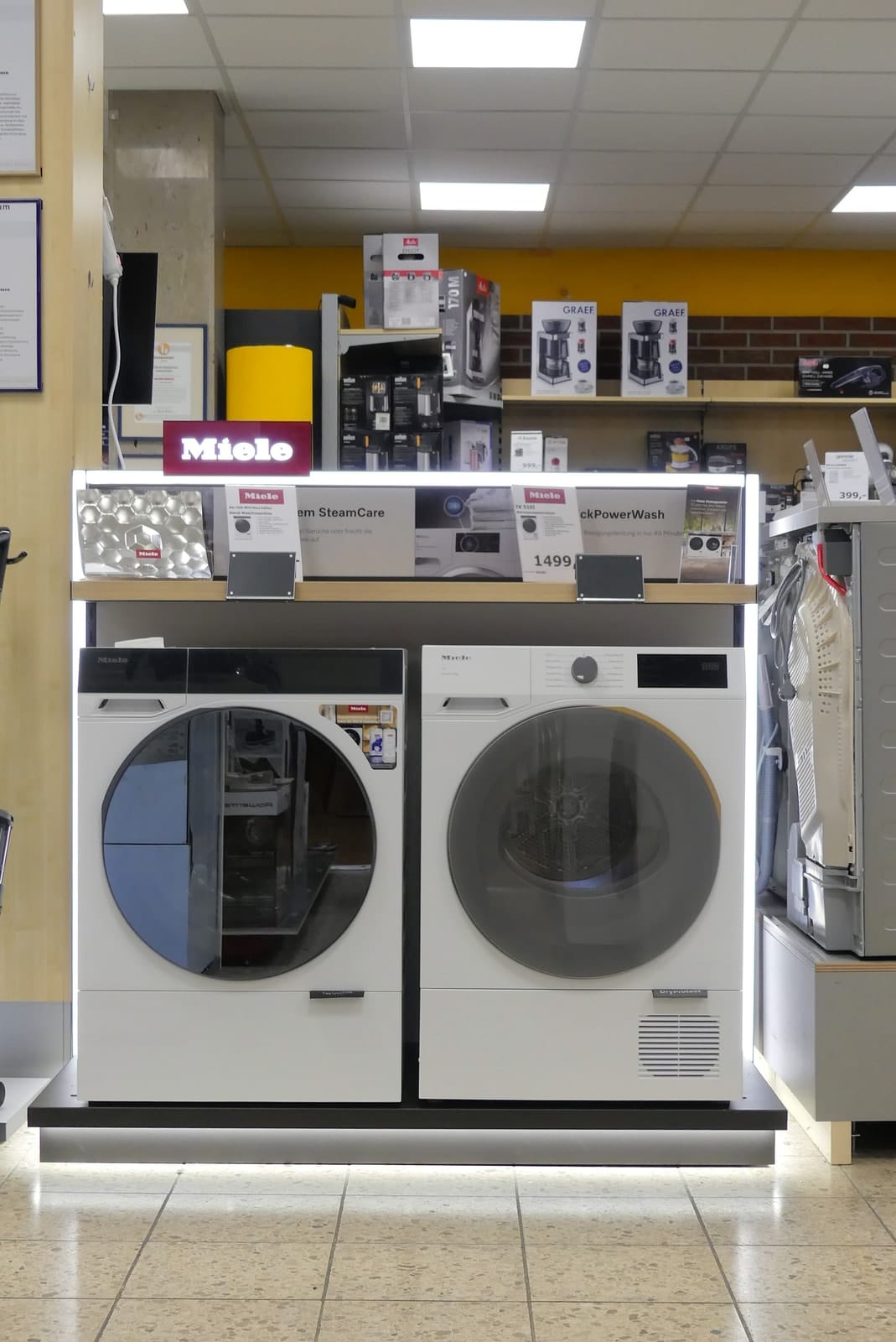 Miele-Waschmaschine und Trockner nebeneinander auf einem beleuchteten Podest